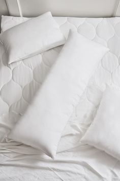 three pillows on top of a bed with white sheets