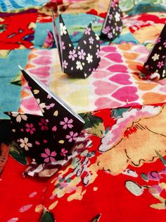 some paper cranes are sitting on a colorful table cloth with flowers and butterflies around them