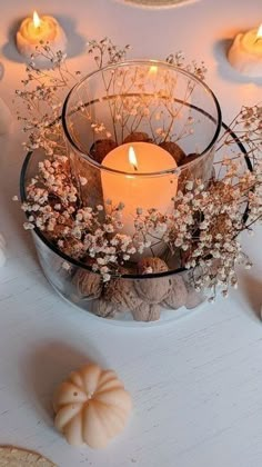 a glass bowl filled with flowers and candles on top of a white table next to cookies