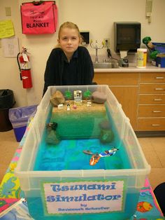 a young boy standing in front of a plastic container filled with sand and water, on top of a table