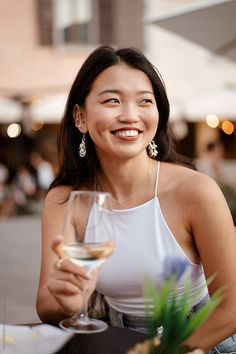 a woman sitting at a table with a glass of wine in front of her smiling