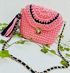 a pink crocheted purse with tassels and a chain around the strap