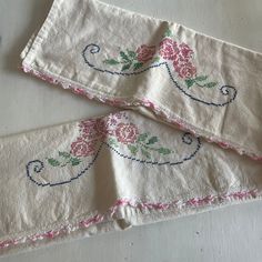 two white napkins with pink flowers on them sitting on a counter top next to each other