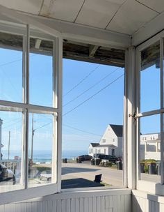 an open window looking out onto the ocean and houses in the distance with cars parked on the street