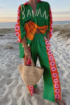 a woman standing on top of a sandy beach next to the ocean holding a straw bag