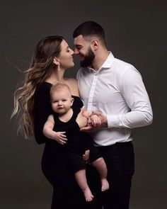 a man and woman holding a baby in front of a gray background with the caption's name on it