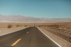 an empty road in the middle of nowhere, with mountains in the backgroud