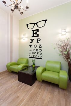 an eye chart wall decal in the corner of a room with green chairs and a coffee table