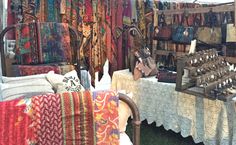 an outdoor market with many different fabrics and rugs for sale on the tables in front of them