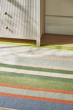 a multicolored striped rug in front of a dresser