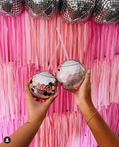 two people holding up pink and silver decorations