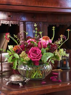 a glass bowl filled with flowers on top of a wooden table next to a mirror