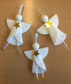 three white angel ornaments with gold stars hanging from strings on a wooden table, ready to be made into christmas ornament decorations