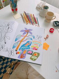 an open book sitting on top of a white table covered in markers and pencils