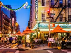 an outdoor cafe with orange umbrellas and people walking down the street in front of it