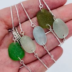 four sea glass necklaces in different colors on a person's hand with silver chain