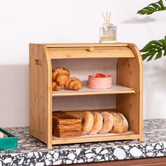 an assortment of breads and pastries on display in a wooden case next to a potted plant