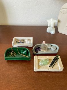 three small trays with jewelry on them sitting on a table next to a vase