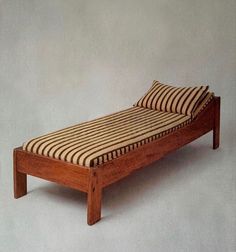 a wooden bed with striped sheets on it's headboard and foot board, against a white wall