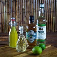 three different types of alcohol sitting on a table next to limes and a bottle