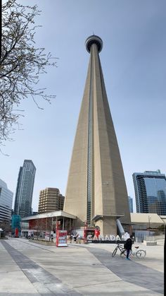 a man riding a bike past a tall tower in the middle of a city with skyscrapers