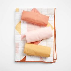 an orange, pink and yellow pillow on top of a white quilted piece of cloth