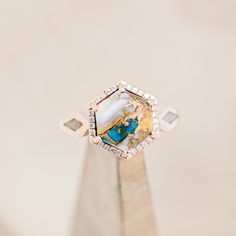 a gold ring with a blue and white stone in the center on top of a wooden stand