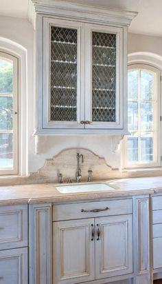 a kitchen with white cabinets and marble counter tops in front of two large windowed windows