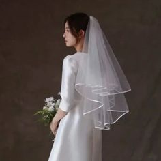 a woman in a white wedding dress with a veil on her head and flowers in her hand