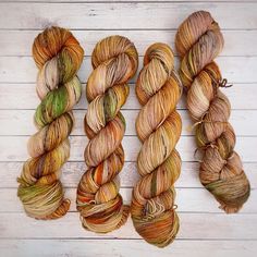 three skeins of yarn on a white wooden surface, one is orange and the other has green