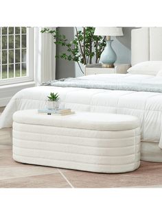 a large white bed sitting in a bedroom next to a table with a potted plant on it