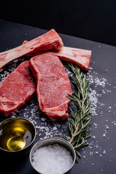 raw steaks and spices on a black surface with salt, pepper, and rosemary