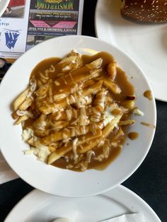 a white plate topped with french fries covered in gravy next to a bun