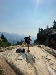 a man standing on top of a large rock next to a backpack in the mountains