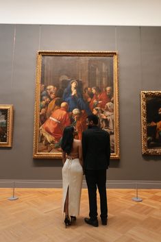 a man and woman standing in front of paintings on the wall at an art museum