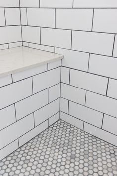 a white tiled bathroom with hexagonal tile flooring and counter top area in the corner