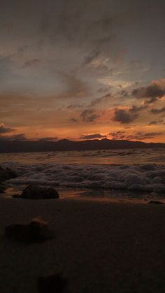 the sun is setting over the ocean with waves coming in