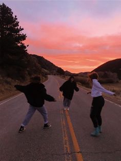 three people skateboarding down an empty road at sunset