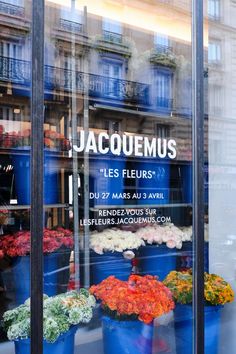 there are many potted flowers in the store front window and behind them is a sign that says jacquemus