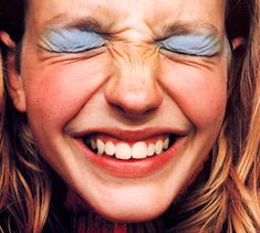 a close up of a person with blue eyes and long blonde hair smiling at the camera