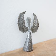 a metal bird sculpture sitting on top of a wooden table next to a white wall