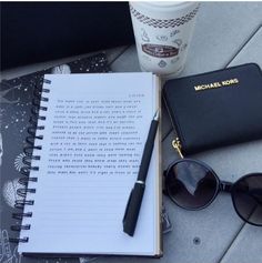 a notepad, pen and sunglasses on the ground next to a coffee cup