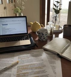 an open laptop computer sitting on top of a wooden desk next to papers and cups