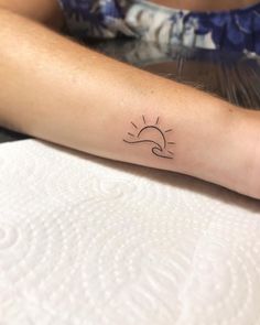 a woman's arm with a small sun and wave tattoo on the left forearm