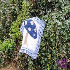 a blue and white mushroom quilt hanging from a tree in front of some green bushes