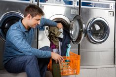 a man sitting on the ground in front of a washer with clothes hanging from it