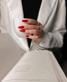 a woman with red nail polish holding an open book