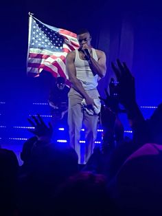 a man standing on top of a stage holding an american flag in front of him