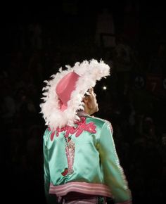 a man in a green jacket and pink hat with feathers on it's head