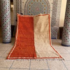 an orange and white rug sitting on top of a tile floor next to tall pillars